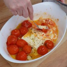 Zdrobirea roșiilor coapte și amestecarea cu brânza feta moale după coacere, pregătind sosul pentru paste.