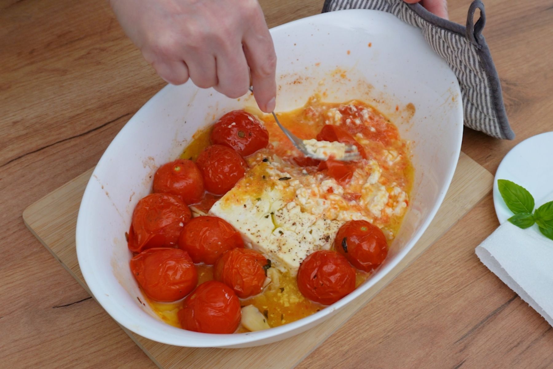 Zdrobirea roșiilor coapte și amestecarea cu brânza feta moale după coacere, pregătind sosul pentru paste.