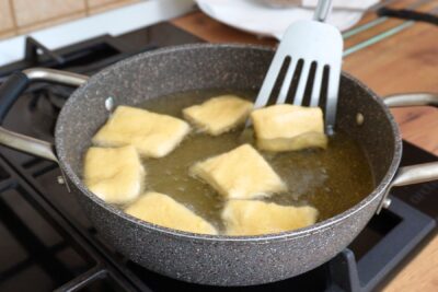 Bucăți de aluat prăjite în ulei încins, rumenite uniform pentru gogoși aurii și pufoase.