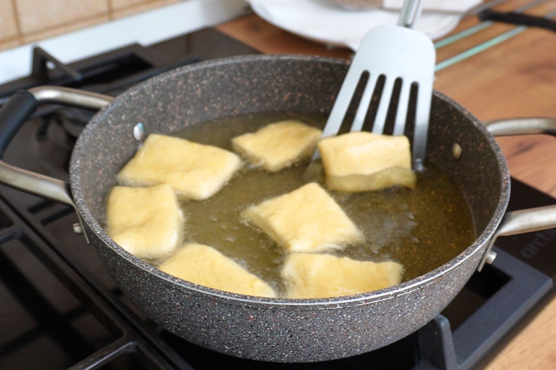 Bucăți de aluat prăjite în ulei încins, rumenite uniform pentru gogoși aurii și pufoase.