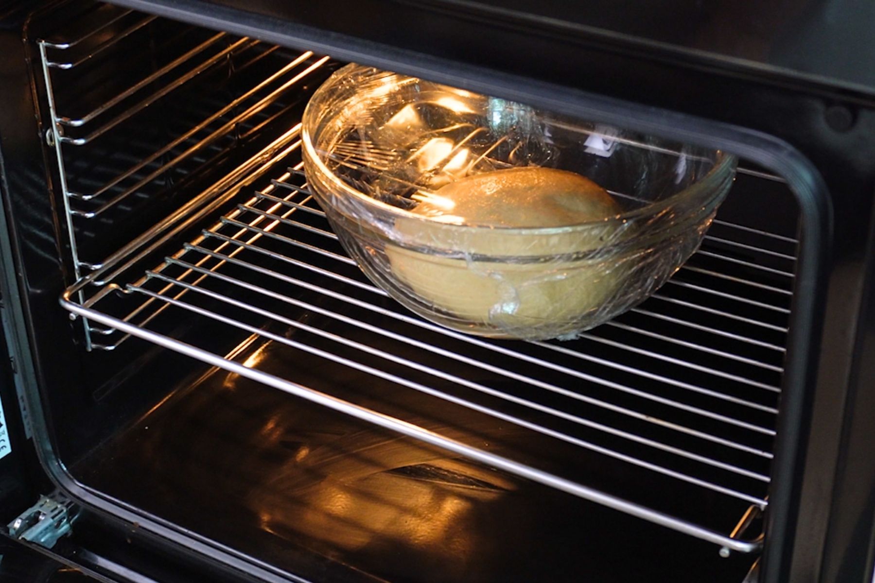 Bol cu aluat de gogoși pus la dospit în cuptorul cald, acoperit cu folie alimentară.