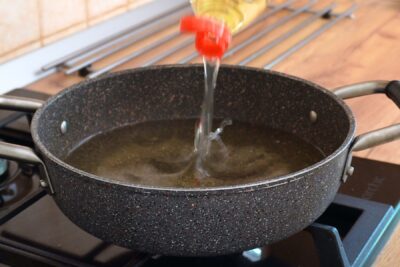 Adăugarea uleiului într-o tigaie adâncă pentru a pregăti gogoșile prin prăjire.