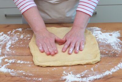 Aluat întins manual pe blatul presărat cu făină, pregătit pentru decupat.