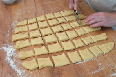 Bucăți de aluat decupate cu rola de patiserie, în forme pătrate pentru gogoși uniforme.