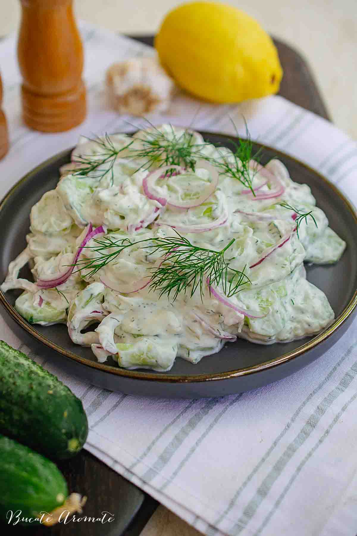Salată de castraveți cu sos cremos de iaurt și mărar, decorată cu rondele de ceapă roșie și mărar verde.