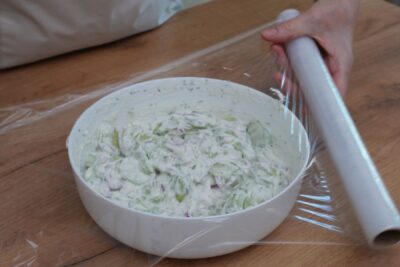 bol cu salata de castraveti cu iaurt si marar acoperit cu folie alimentara pentru frigider