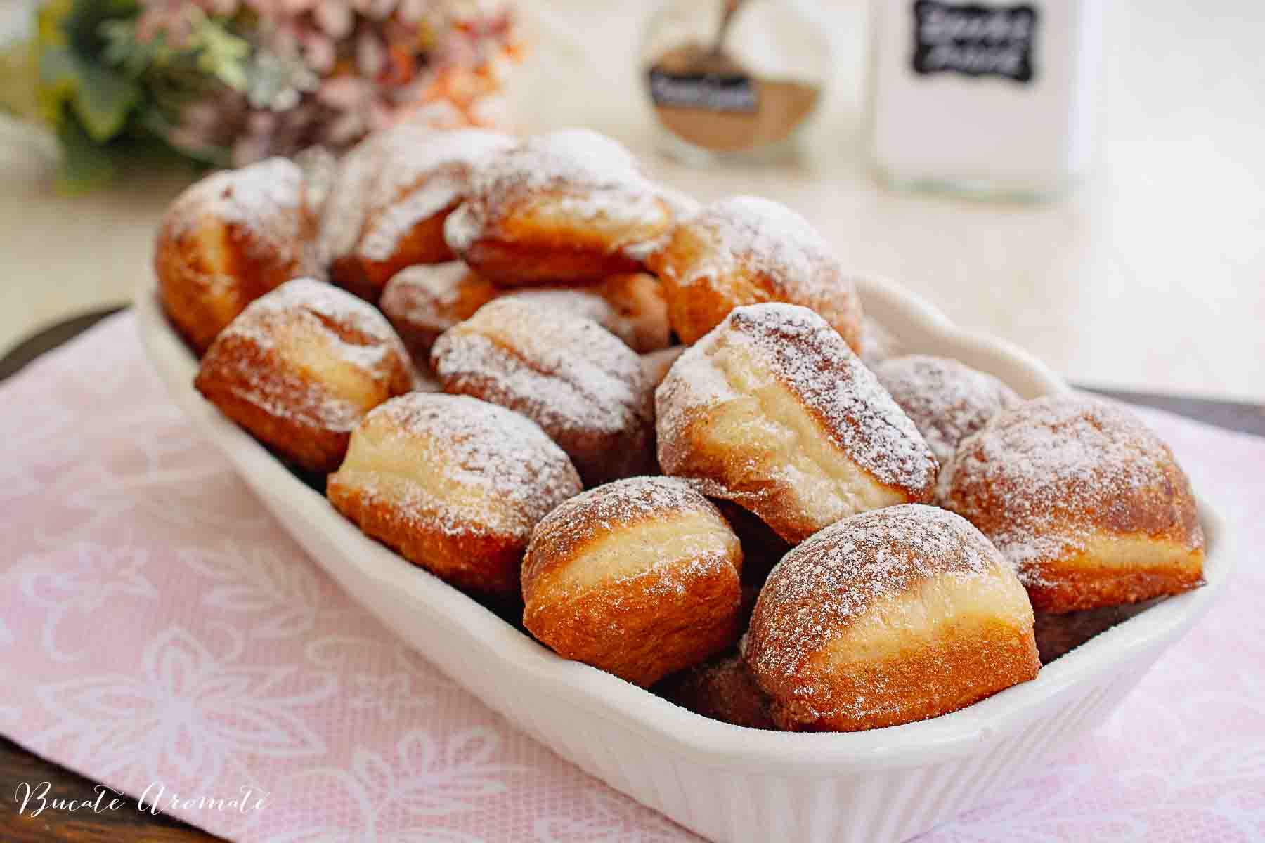 Gogoși prăjite moi și pufoase așezate pe platou de servire alb peste fața de masă