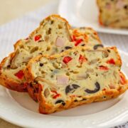 Farfurie alba cu felii de chec aperitiv cu iaurt. In sectiune se vad masline, cuburi de legume, branzeturi si sunca