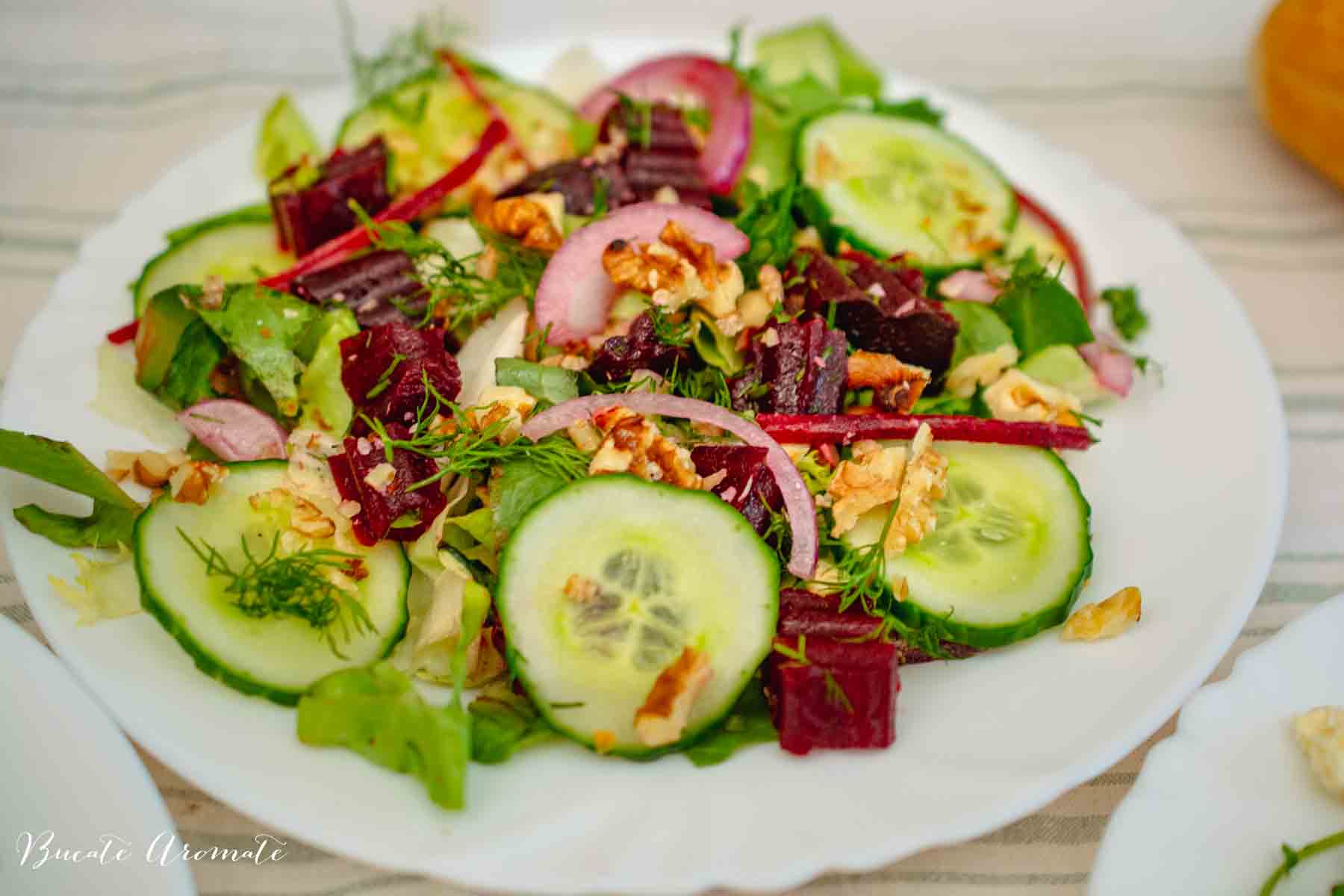 salata de sfecla rosie fiarta cu castraveti, marar si nuci servita pe farfurie alba