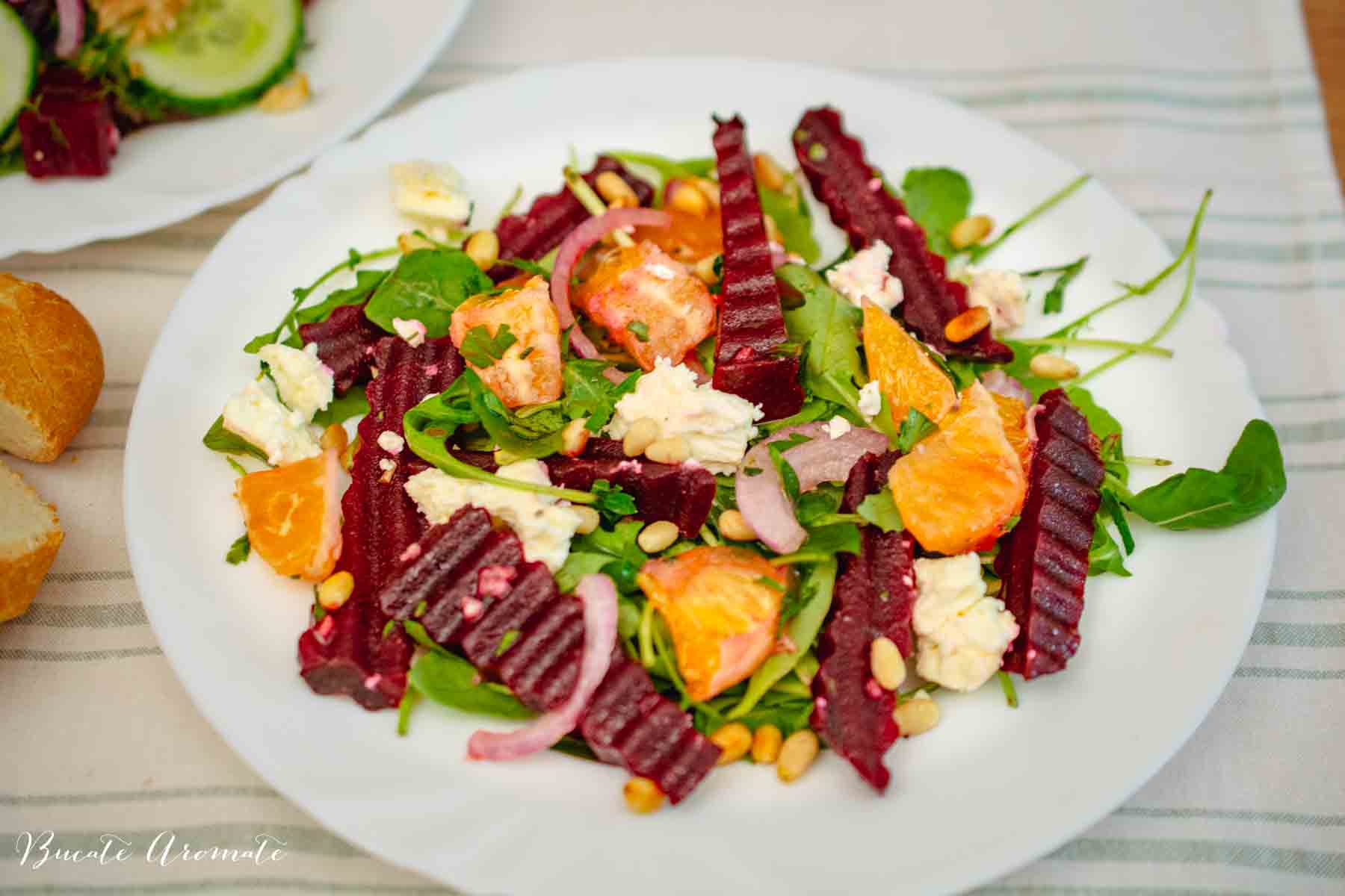 farfurie alba cu salata de toamna cu sfecla, portocale si rucola, presarata cu branza feta si muguri de pin