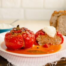 Gogoșari copți umpluți, gata de servit, în sos de roșii, cu felii de pâine și smântână