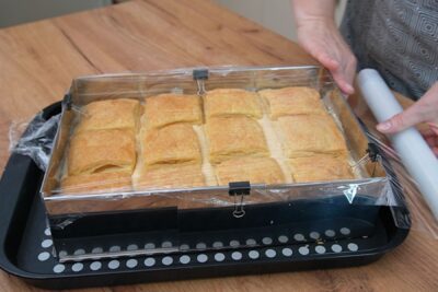 Cremșnit de casă montat în tavă, acoperit cu folie alimentară pentru răcire la frigider.