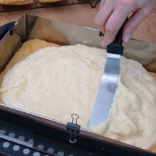 Crema fină de vanilie turnată și întinsă peste foaia de cremșnit făcută în casă.