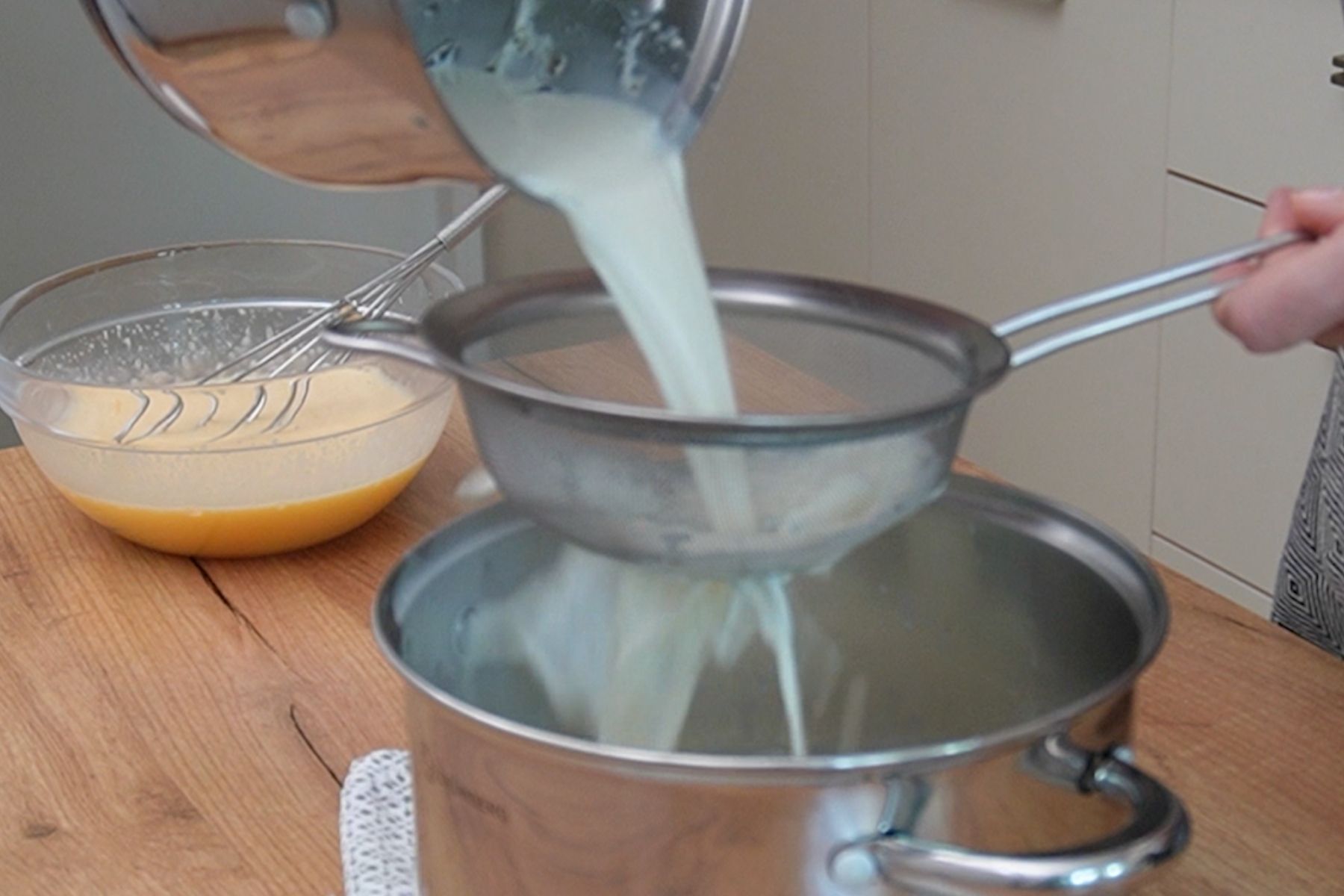 Lapte infuzat cu vanilie strecurat prin sită fină pentru crema de vanilie.