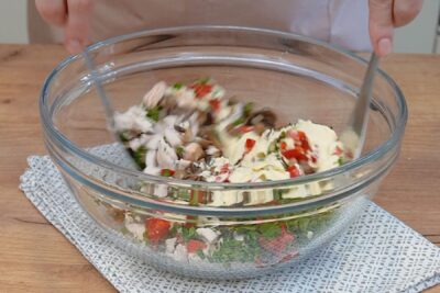 salata cu pui, ciuperci si gogosari amestecata cu spatula in castron transparent