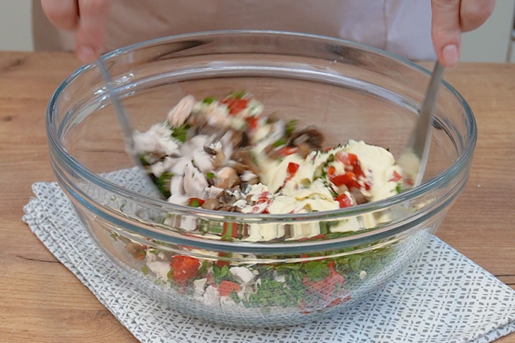 salata cu pui, ciuperci si gogosari amestecata cu spatula in castron transparent