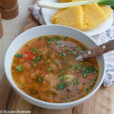 Ciorbă de varză dulce de post cu borș și legume, presărată cu pătrunjel proaspăt, servită cu mămăligă.