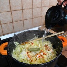 Turnare apă fierbinte peste varza tocată cu boia și dafin, în prepararea ciorbei de varză dulce de post cu borș.