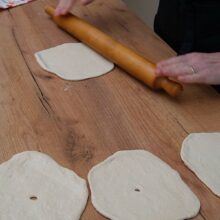 Bucăți de aluat întinse rotund, cu sucitorul, fiecare cu o gaură mică în mijloc, pregătite de prăjit