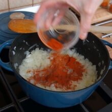 Boia roșie adăugată peste ceapa aurie într-o cratiță, pentru gust autentic de gulaș