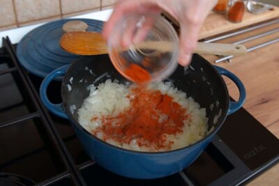 Boia roșie adăugată peste ceapa aurie într-o cratiță, pentru gust autentic de gulaș