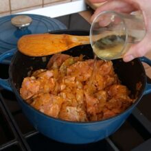 Pahar cu vin alb turnat în cratiță cu carne și ceapă, pentru un gulaș aromat și fraged