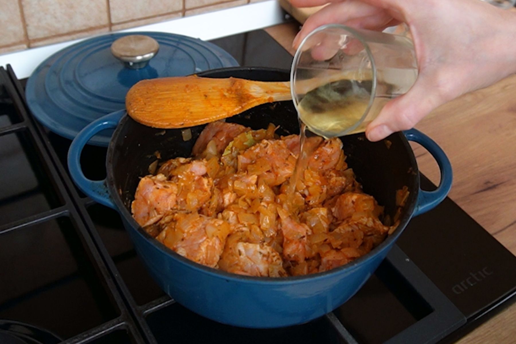 Pahar cu vin alb turnat în cratiță cu carne și ceapă, pentru un gulaș aromat și fraged