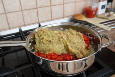 Vinete coapte și tocate adăugate peste ardei și ceapă în tigaie pentru zacuscă de post