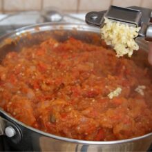 Usturoi proaspăt adăugat la final în zacusca rapidă de vinete și ardei copți