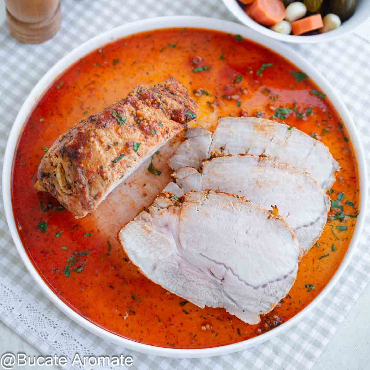 Felii de mușchi de porc la cuptor, împănat cu usturoi, servit în sos roșu aromat