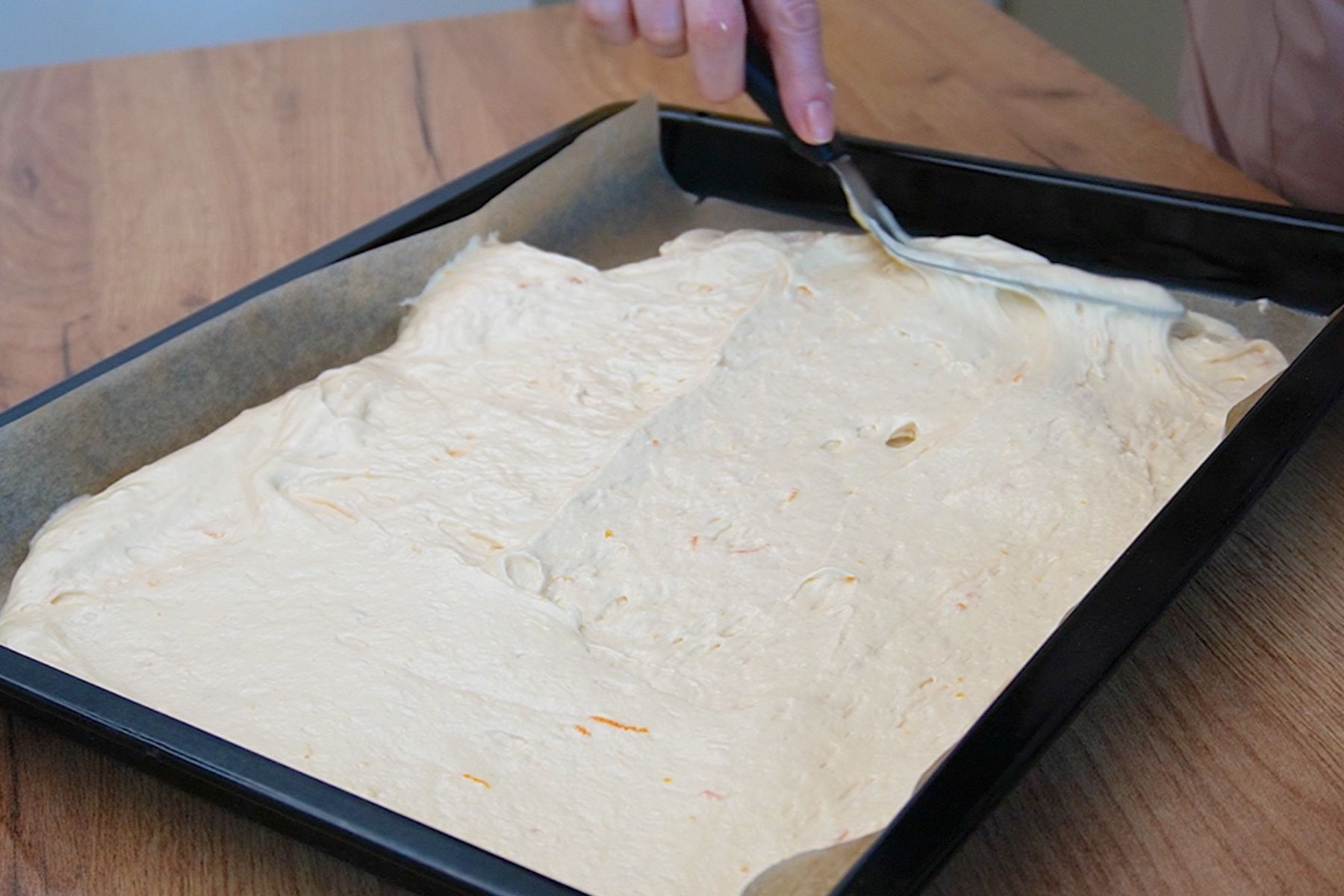 Compoziția de pandișpan pentru prăjitura Diplomat la tavă este întinsă și nivelată într-o tavă tapetată cu hârtie de copt