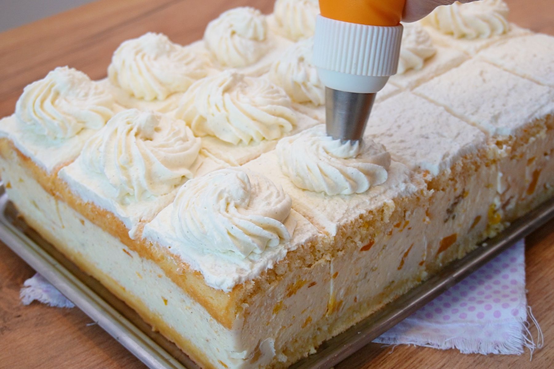 Frișca bătută se pune cu poșul în rozete decorative pe suprafața prăjiturii Diplomat, înainte de adăugarea fructelor