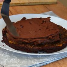 Cremă de ciocolată de post întinsă peste primul blat de cacao la asamblarea tortului de post cu ciocolată