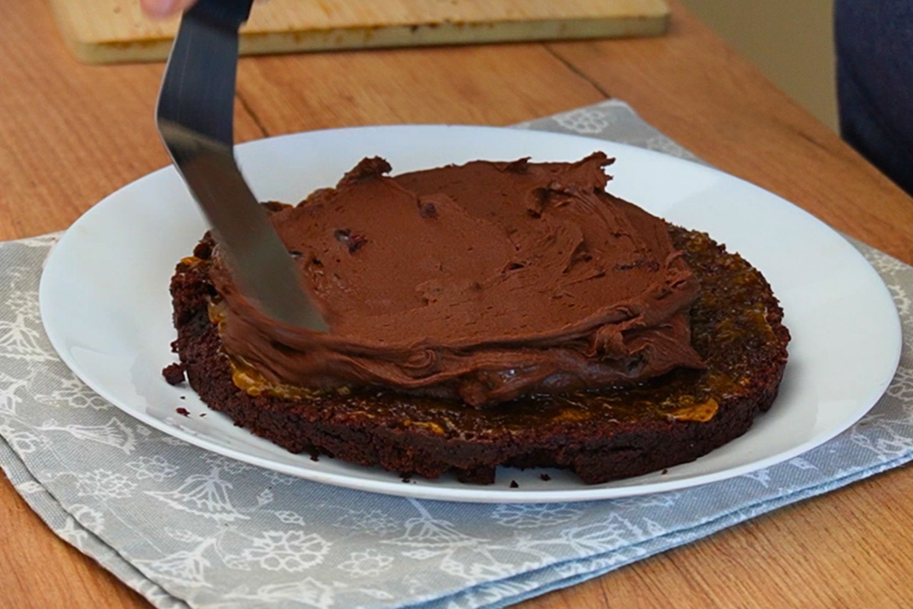 Cremă de ciocolată de post întinsă peste primul blat de cacao la asamblarea tortului de post cu ciocolată