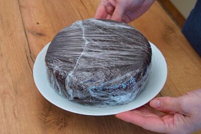 Blat de tort de post cu ciocolată învelit în folie alimentară și lăsat la răcit înainte de tăiere