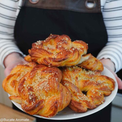 Covrigi polonezi însiropați, rumeni și pufoși, așezați pe o farfurie albă și ținuți în mâini, fotografie de aproape.