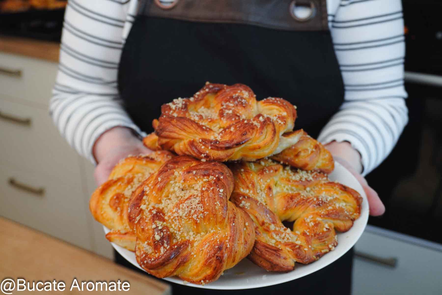 Covrigi polonezi însiropați, rumeni și pufoși, serviți pe o farfurie albă, ținută în mâini.