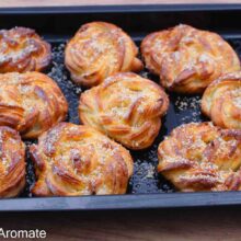 Covrigi polonezi însiropați după coacere, așezați în tavă și presărați cu nucă măcinată.