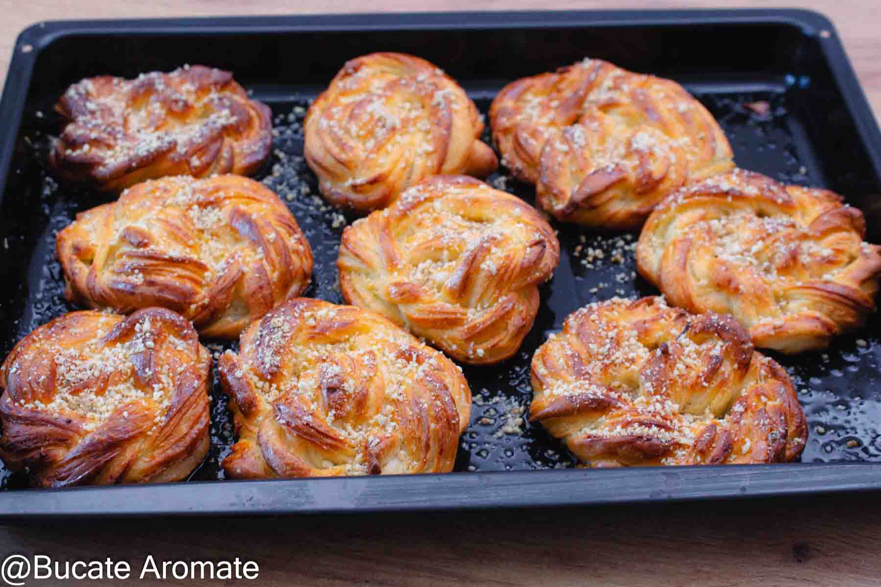 Covrigi polonezi însiropați după coacere, așezați în tavă și presărați cu nucă măcinată.