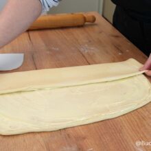 Împăturirea aluatului uns cu unt pentru covrigi polonezi, pe blatul de lucru