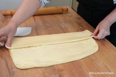 Împăturirea aluatului uns cu unt pentru covrigi polonezi, pe blatul de lucru