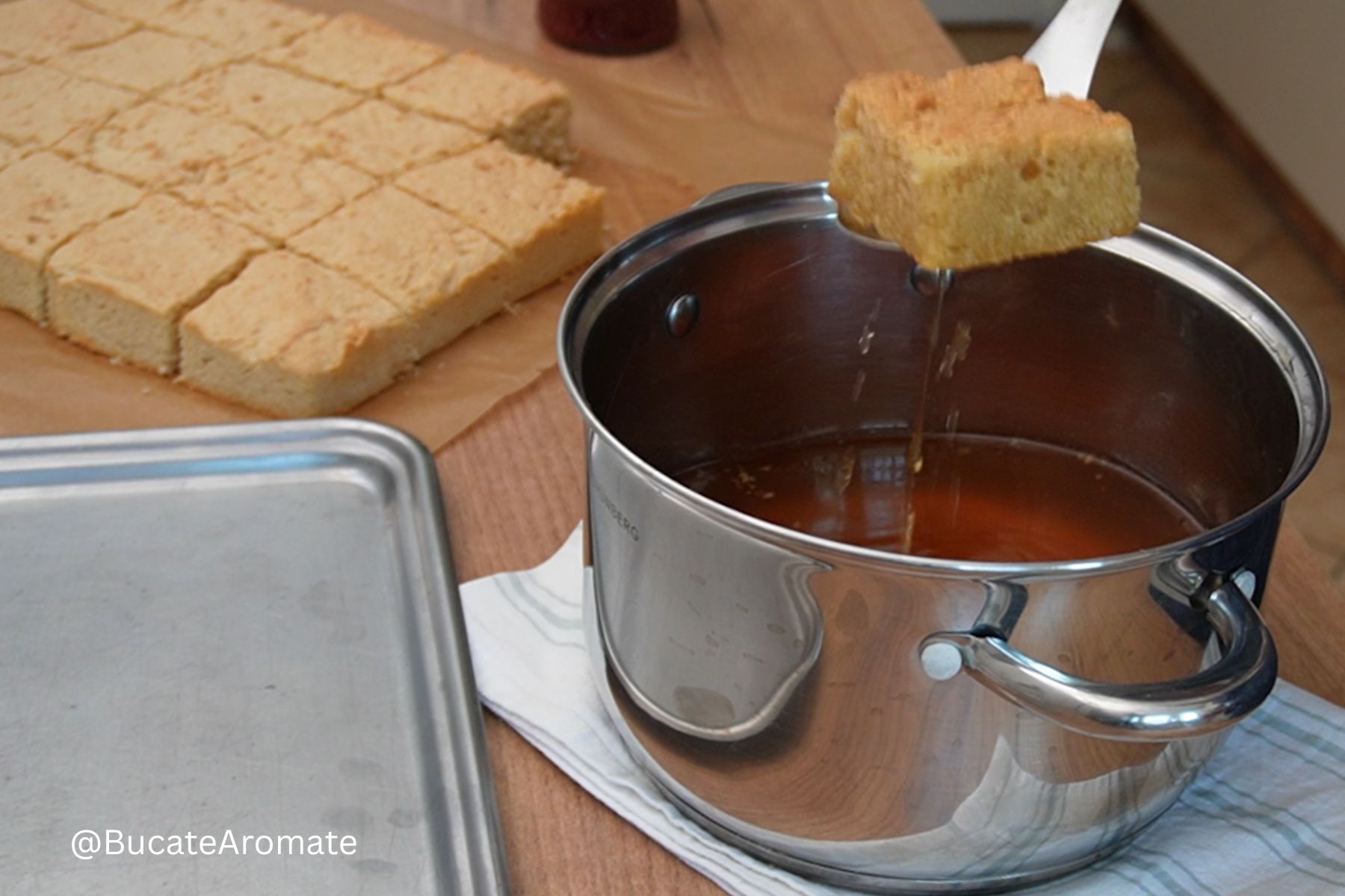 O bucată de blat pentru savarine cu pesmet la tavă este trecută prin sirop aromat, înainte de montare.