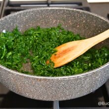 Spanac sotat în unt într-o tigaie adâncă, înainte de adăugarea sosului de lapte