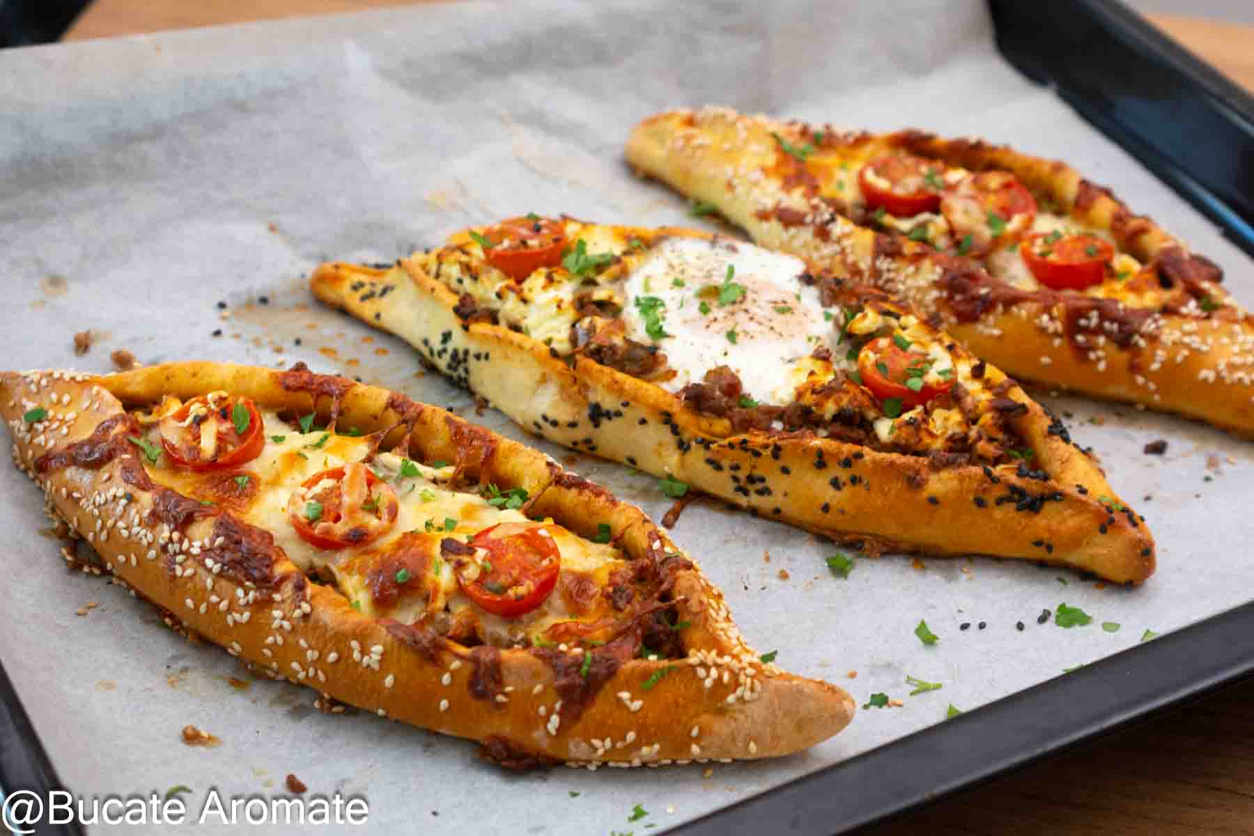 Pide turcești cu carne tocată de vită, telemea, ou și roșii cherry, cu margini rumenite și semințe de susan.