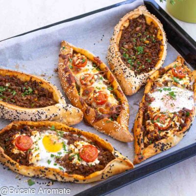Pide turcești cu carne tocată de vită, ou, telemea, roșii cherry și margini cu susan, coapte în tavă.