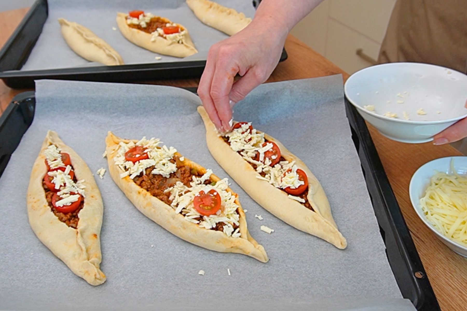 Pide turcești cu carne tocată de vită decorate cu telemea, cașcaval ras și roșii cherry înainte de coacere.