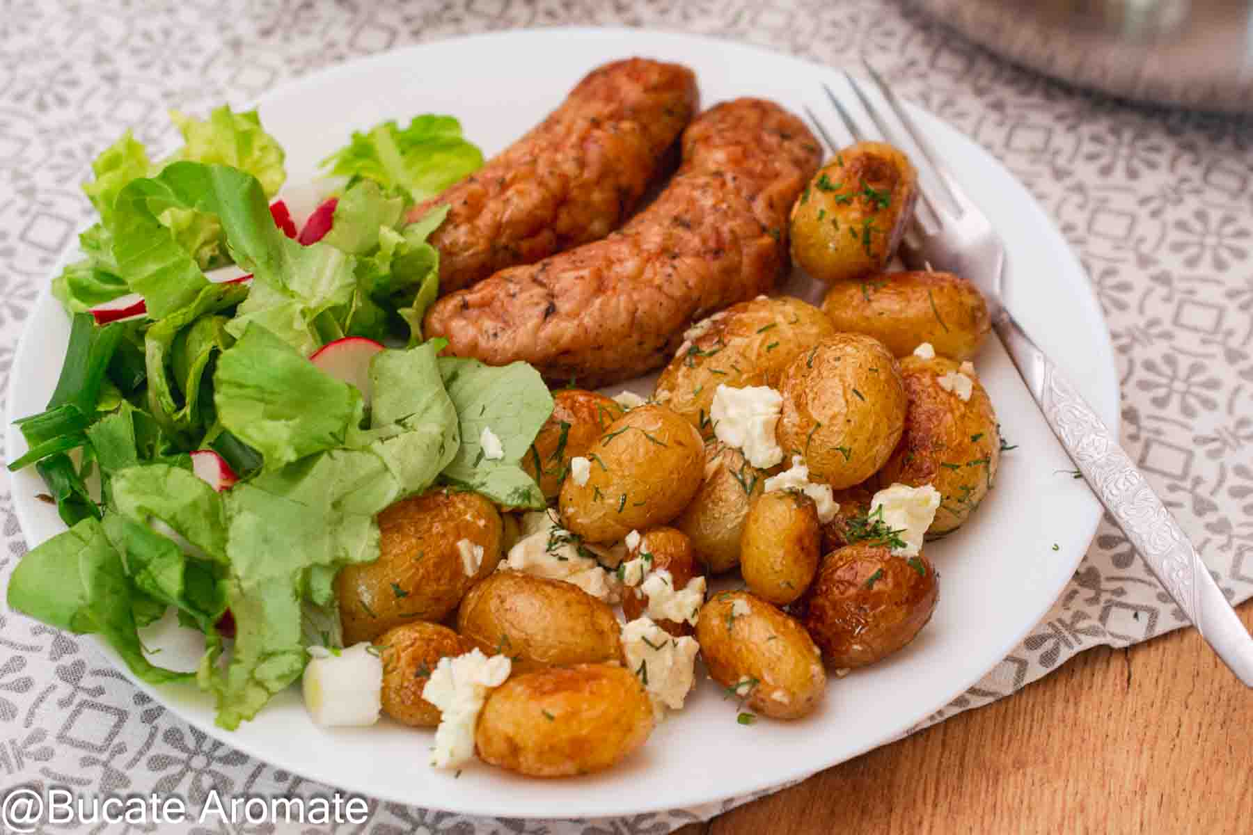 Farfurie cu cartofi noi rumeniți la tigaie, brânză, salată verde și cârnăciori de pui.