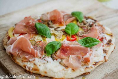 Pizza rapidă la tigaie cu praf de copt, servită pe tocător, cu blat subțire, legume călite, cașcaval topit și prosciutto crudo.