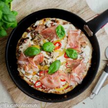Pizza la tigaie fără drojdie, cu blat subțire, cașcaval topit, prosciutto crudo, ardei, ciuperci și frunze de busuioc.