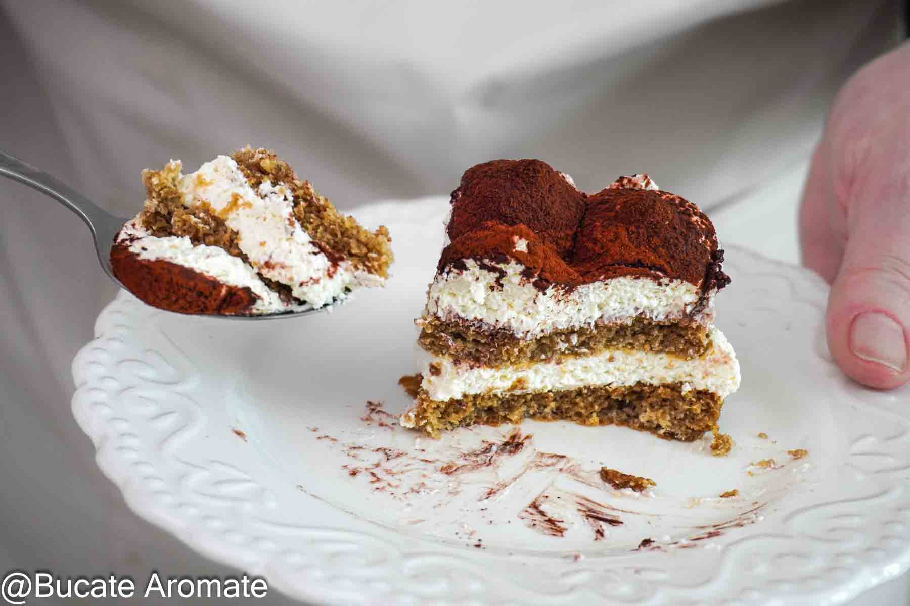 Felie de prăjitură Tiramisu cu blat de casă, cremă de mascarpone și cacao, servită pe farfurie cu lingurița